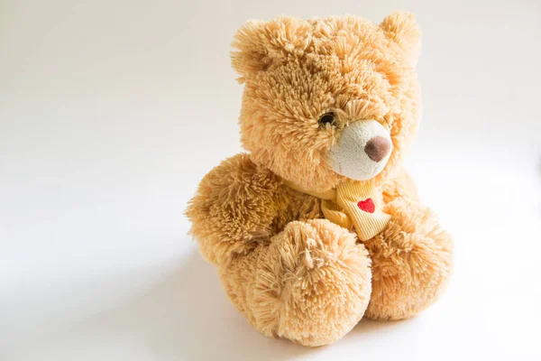 Soft Teddy bear with long light brown fur and a red heart on a scarf around his neck. Valentine\'s day gift, children\'s toy. White background, space for text