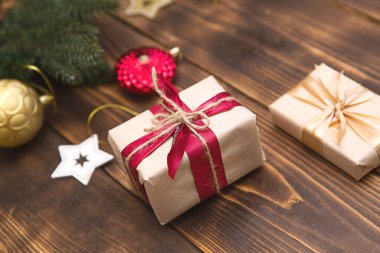 Açık kağıda noel hediyesi konan bir kutu ahşap bir arka planda kırmızı bir kurdeleyle süslenir. Noel ağacı kolyesi, boncuklar, çelenkler. Yeni yıl. Metin için boşluk