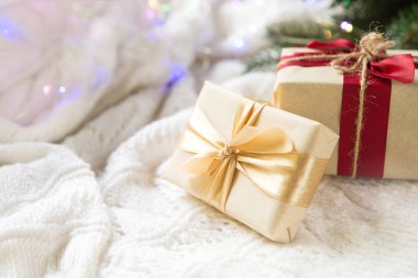 Işık kağıdında noel hediyesi olan bir kutu beyaz örülmüş bir arka planda altın bir kurdeleyle süslenir. Noel ağacı kolyesi, yeşil dallar, ışık çelenkleri. Yeni yıl. Metin için boşluk