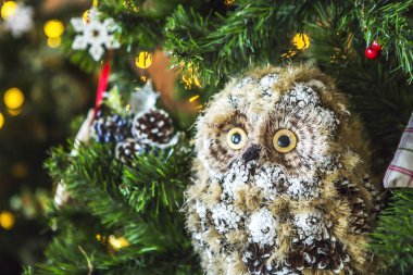 Baykuş oyuncaklar - toplar, Noel ağaçları, kar taneleri, dekore edilmiş yeşil bir Noel ağacı meyveleri. Arka planda başka bir Noel ağacı, bir kurabiye evi ve sarı ışık dekore edilmiş