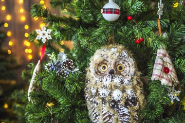 Baykuş oyuncaklar - toplar, Noel ağaçları, kar taneleri, dekore edilmiş yeşil bir Noel ağacı meyveleri. Arka planda başka bir Noel ağacı, bir kurabiye evi ve sarı ışık dekore edilmiş