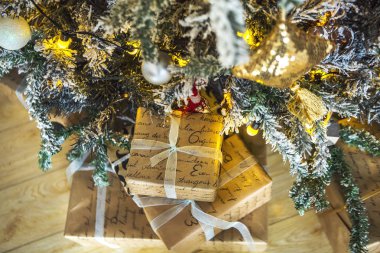 Hediyeler Noel oyuncaklar ve mumlarla süslenmiş yeşil Noel ağacının altında kırmızı ve beyaz ambalajın Paketli. Arka planda bir kurabiye evi ise sarı Noel ışıkları