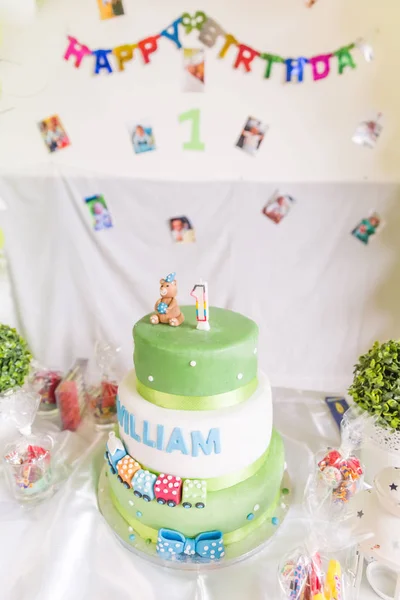 Green and White Birthday Cake with One Year Old Candle with Happy Birthday Banner in the Background