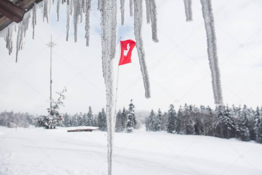 Swiss Flag Floating behind Chalet Stalactites in Winter