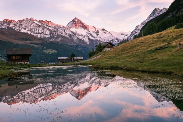 Sunset over Snowy Mountains and Wood Chalet Reflecting in Altitude Lake