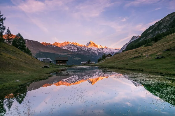 Sunset over Snowy Mountains and Wood Chalet Reflecting in Altitude Lake