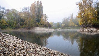 Sonbahar, puslu sabah parkta etrafında ağaçlar büyümek bir su birikintisi. Taşlı shore.