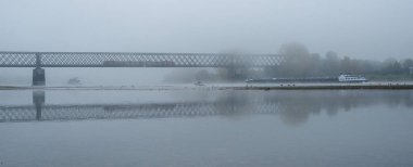 Sisli sonbahar sabahı Almanya'da Ren, eski bir demiryolu köprüsü uzakta akan bir mavna Nehri üzerinde.