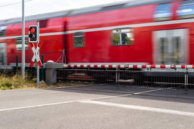 Korunan demiryolu geçişi ile kapalı engelleri ve kırmızı ışıkta geçen bir yolcu treni.
