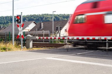 Korunan demiryolu geçişi ile kapalı engelleri ve kırmızı ışıkta geçen bir yolcu treni.