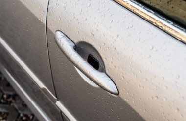 Yağmur damlaları gümüş bir araba görünür yan ön kapı kolu.