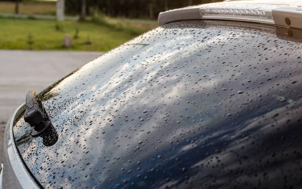 Raindrops on a silver car on the rear black window of the car with visible rear wiper.