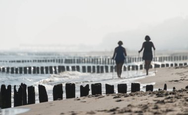Kolobrzeg, Polonya 28 Juli 2018. İki kadın Nordik yürüyüş ve ahşap dalgakıranlar pratik puslu sabah sahilde Lehçe görünür bulanık.