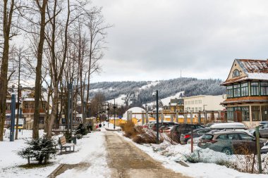 Zakopane, Polonya - 22 Şubat 2019. City park kapsamında kar, görünür kaldırım, araba park yeri ve kentsel binalar ile. Arka planda dağlar kar ve bulutlu gökyüzü ile kaplı.