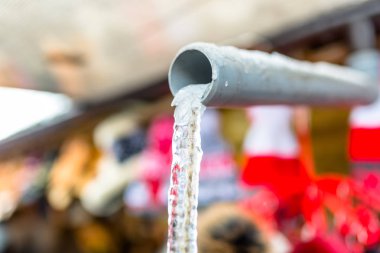 Bir dizge içinde plastik bir boru aracılığıyla çatıdan akan su donmuş.