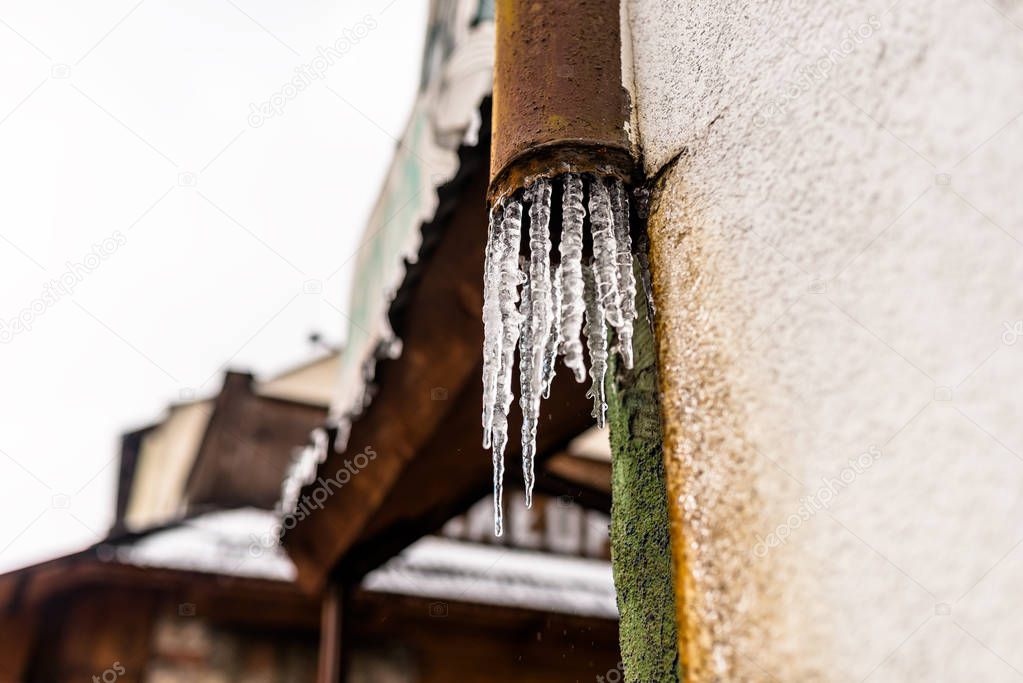 Frozen water flowing from the roof through a damaged, rusty, metal gutter that is on the facade of the building.
