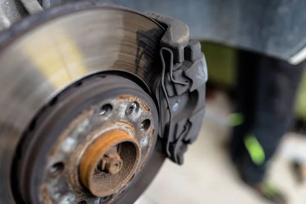 Front brake discs with caliper and brake pads in the car, on a car lift in a workshop.