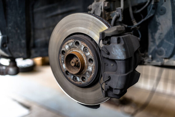 Передние тормозные диски с суппортом и тормозными колодками в машине, на автомобильном подъемнике в мастерской
.