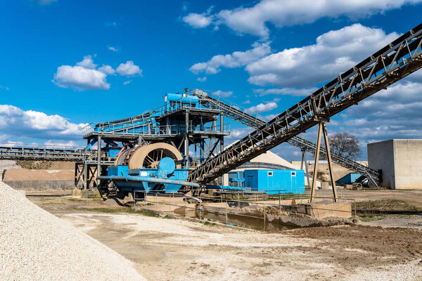 Machine for transferring gravel, spoil for transport belts on blue sky at an industrial cement plant.