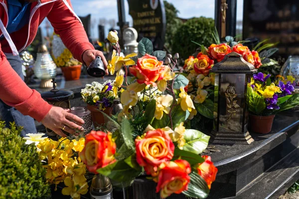 人工花とろうそく足は 墓地の墓石の上に横たわっています 男性の目に見える手 — ストック写真