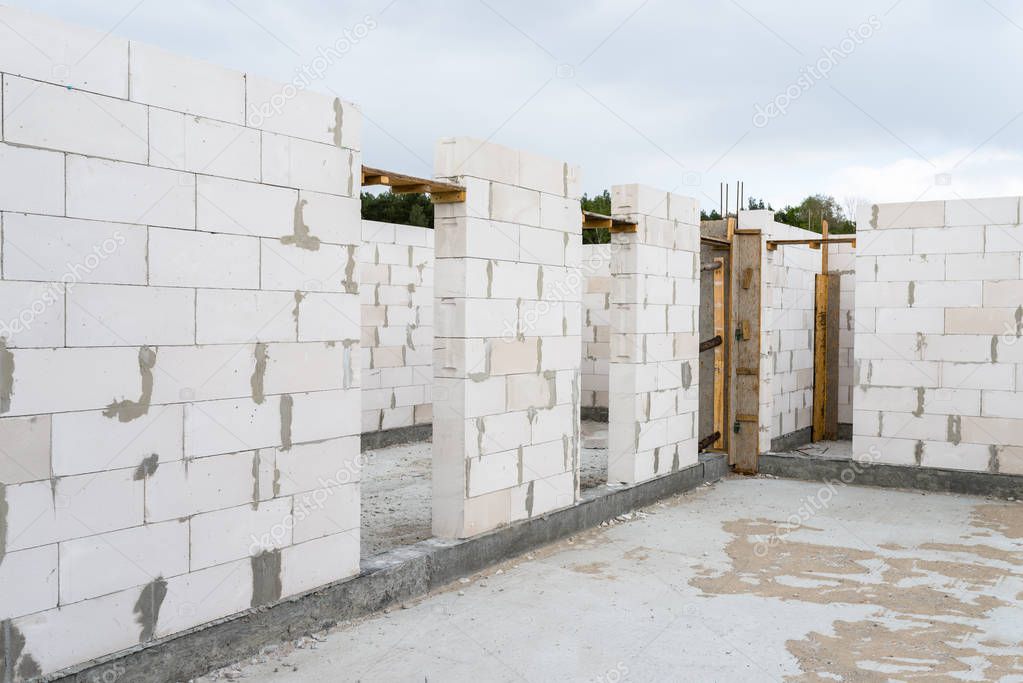 The walls of a house built of white brick with reinforced concrete pillars at the end of which there are ribbed rods, wooden formwork visible from the pillars.