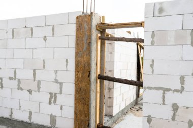 Sonunda nervürlü çubuklar, sütunlardan görülebilen ahşap kalıplar bulunan betonarme sütunlarla beyaz tuğladan yapılmış bir evin duvarları.