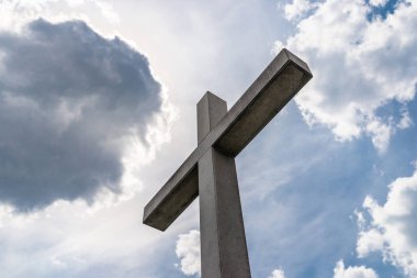 Beyaz bulutlarla mavi bir gökyüzüne karşı mezarlıkta büyük bir beton haç.