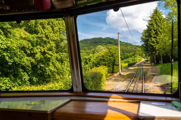 A view from the window of a moving train, visible tracks, trees and blue sky with white clouds.