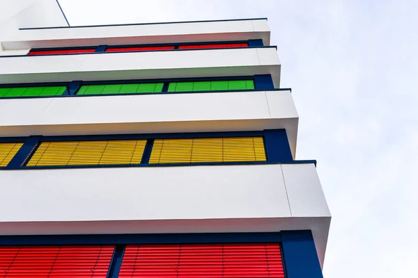 Elevation of a modern office building with different colors of blinds on each floor.