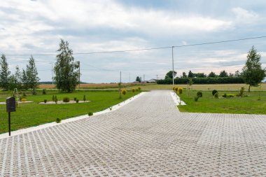 Renkli çakıl taşları ile dolu açık çalışma beton kaldırım yapılmış özelliği içine araba için giriş, çevresinde yeşil çim ve küçük ağaçlar.
