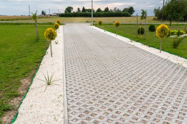 Renkli çakıl taşları ile dolu açık çalışma beton kaldırım yapılmış özelliği içine araba için giriş, çevresinde yeşil çim ve küçük ağaçlar.