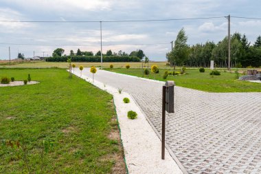 Renkli çakıl taşları ile dolu açık çalışma beton kaldırım yapılmış özelliği içine araba için giriş, çevresinde yeşil çim ve küçük ağaçlar.