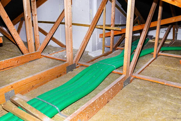 Home energy recovery ventilation, visible system of green flexible pipes for air transport, spread over the roof trusses with visible rock wool.