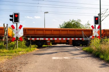 Closed barrier at the railroad crossing with red warning lights on, visible blurred red wagons in motion. 