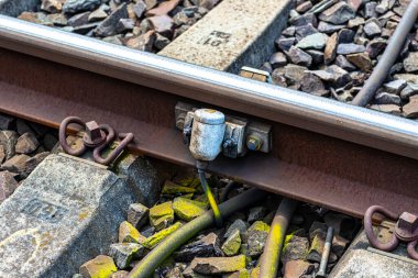 Railroad tracks lying on concrete sleepers, filling large pieces of rock, close-up on the axle counter detection unit. clipart
