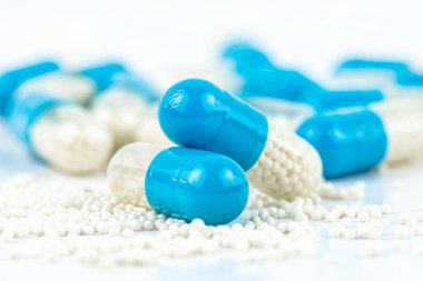 Beyaz granüllü mavi jelatin kapsüller, beyaz arka planda izole edilmiş ve etrafa saçılmış granüller, makro çekim.