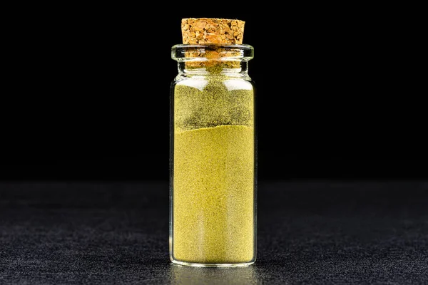 Macro shot of ground lovage leaves spice in a small glass bottle closed with a cork, isolated on a black background.