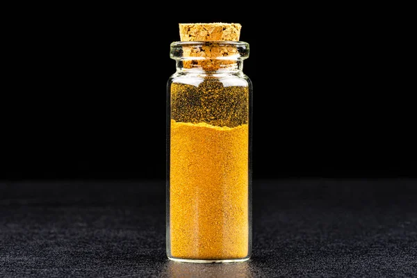 Macro shot of ground Ceylon Cinnamon spice in a small glass bottle closed with a cork, isolated on a black background.