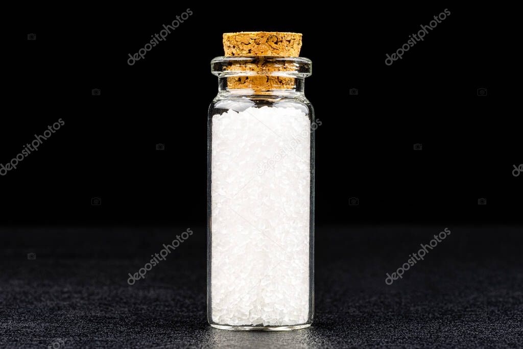 Macro shot of not ground sea salt in a small glass bottle closed with a cork, isolated on a black background.