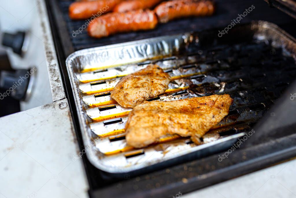 Two chicken fillets lying on an aluminum tray on a gas grill.