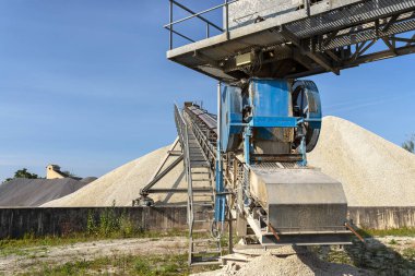 Endüstriyel çimento fabrikasında mavi gökyüzüne çakıl yığınları üzerinde birbirine bağlı taşıma bantları sistemi.