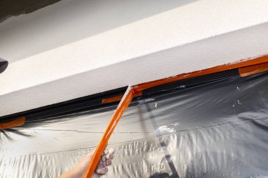 Pencere pervazına yeni uygulanmış silikon alçı tabakası. Pencere siyah folyoyla kaplanmış. Turuncu bandı söküyor..