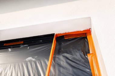 Pencere pervazına yeni uygulanmış silikon alçı tabakası. Pencere siyah folyoyla kaplanmış. Turuncu bandı söküyor..