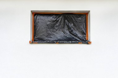 Evin duvarına yeni uygulanmış beyaz silikon alçı tabakası. Pencere siyah folyoyla kaplanmış..