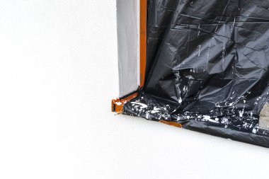 Evin duvarına yeni uygulanmış beyaz silikon alçı tabakası. Pencere siyah folyoyla kaplanmış..