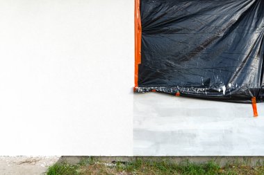 Evin duvarına yeni uygulanmış beyaz silikon alçı tabakası. Pencere siyah folyoyla kaplanmış..