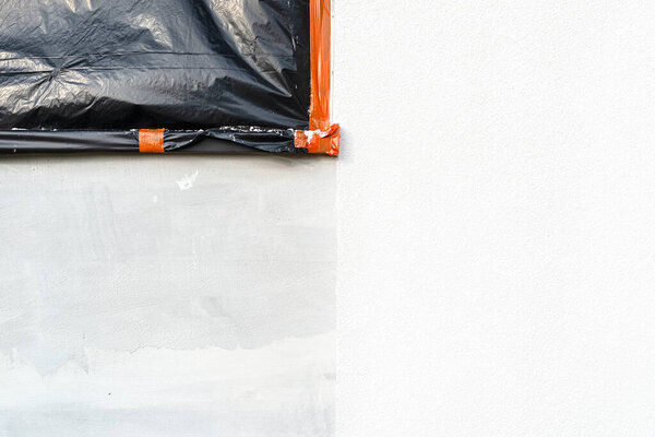 A newly applied layer of white silicone plaster on the wall of the house, the window is secured with black foil.