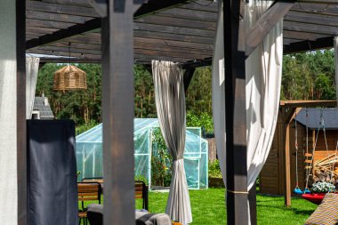 Evin arkasındaki teras görünür perdeleri ve dekoratif LED ışıkları olan kirişlerden yapılmıştır..