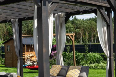 Evin arkasındaki teras görünür perdeleri ve dekoratif LED ışıkları olan kirişlerden yapılmıştır..