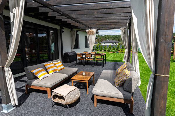 The terrace behind the house is made of beams, with chairs and a table visible.